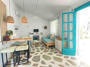 A compact living space with a kitchenette, a dining area with stools, a sofa, and a large window with a blue door.