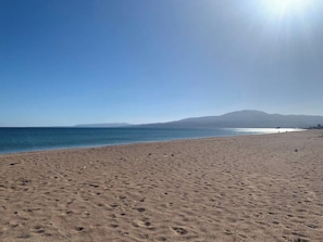 A wide sandy beach with footprints, a clear blue sky, and distant mountains.