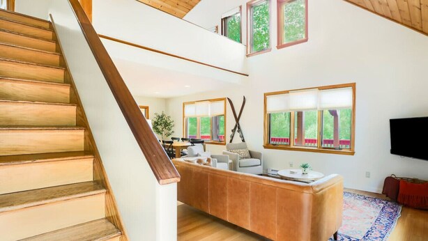 A modern interior with a wooden staircase, a central seating area, and large windows.