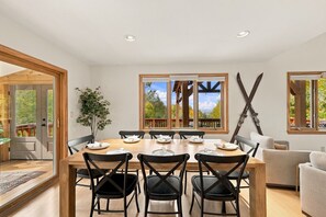 A dining room with a large wooden table, six chairs, and a view of the outdoors through large windows. - Mountain Views, Hot Tub near Hiking, Ski & Santa`s Village (Jefferson)