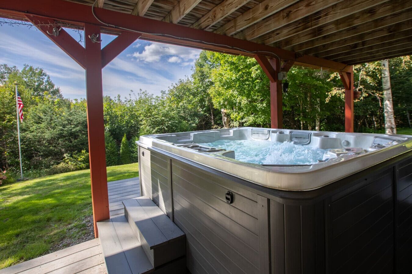 Ett bubbelbad under en träpergola, med en gräsyta och träd i bakgrunden.