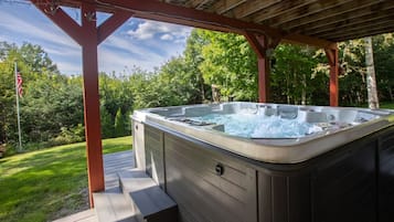 Ett bubbelbad under en träpergola, med en gräsyta och träd i bakgrunden.