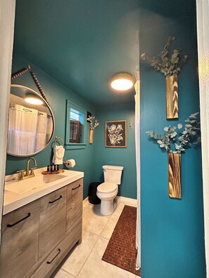 Ein Badezimmer mit einer türkisblauen Wand, einem weißen Waschbecken mit goldfarbenen Armaturen, einer Toilette und einem Spiegel.