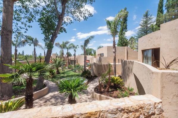 A courtyard with palm trees, a stone pathway, and modern buildings with large windows. - La María Hotel Boutique (Chacras de Coria)