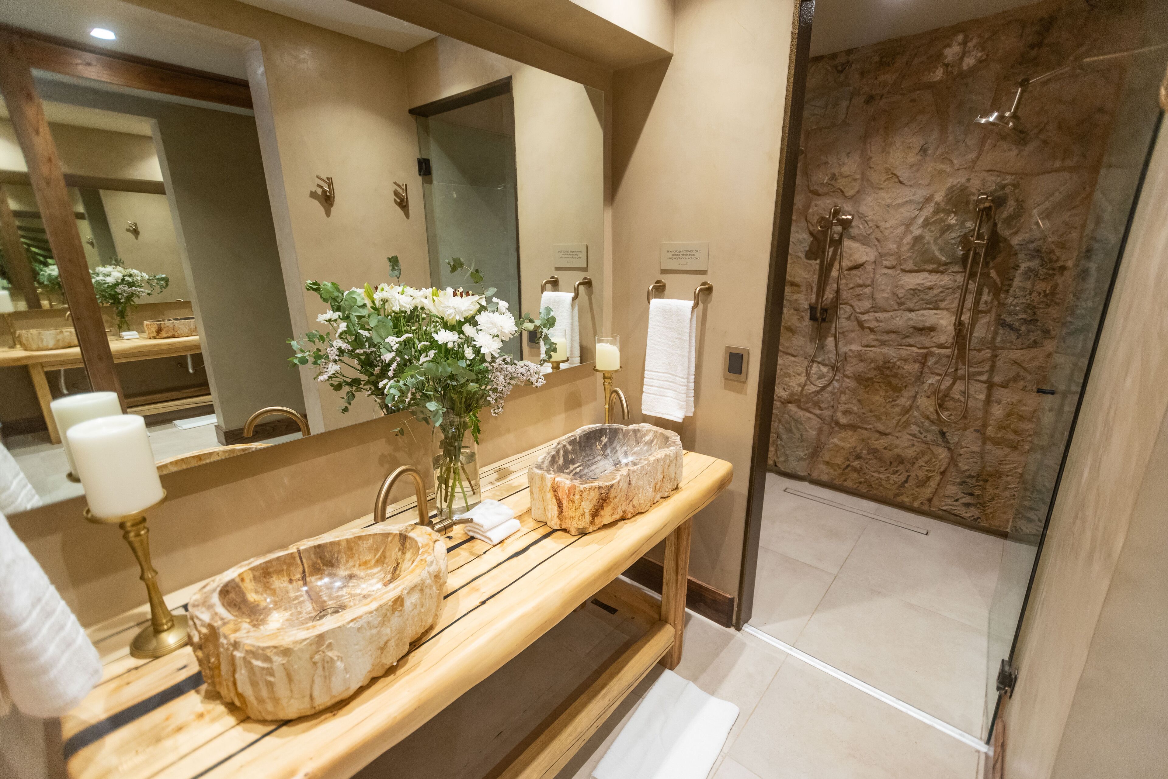 A bathroom with a stone sink, a mirror, a vase with flowers, and a shower area.