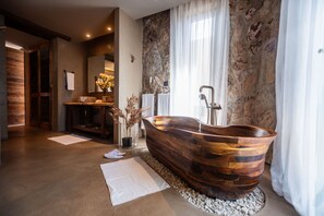 Un baño moderno con una bañera de madera, una pared de piedra y un espejo grande.