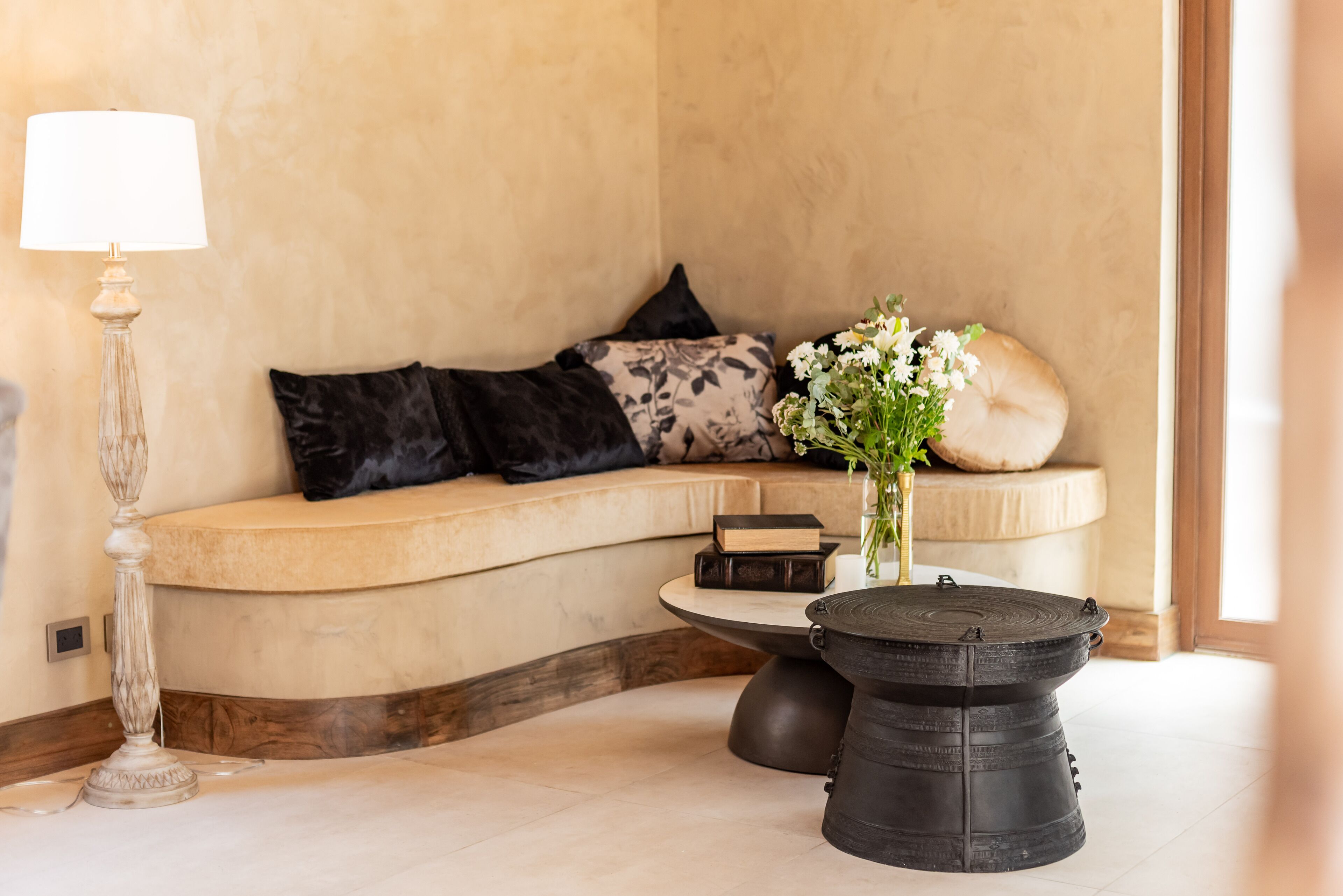 A cozy seating area with a curved sofa, a small round table, a lamp, and a vase with flowers.