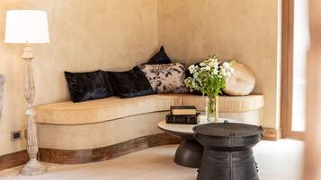 A cozy seating area with a curved sofa, a small round table, a lamp, and a vase with flowers.
