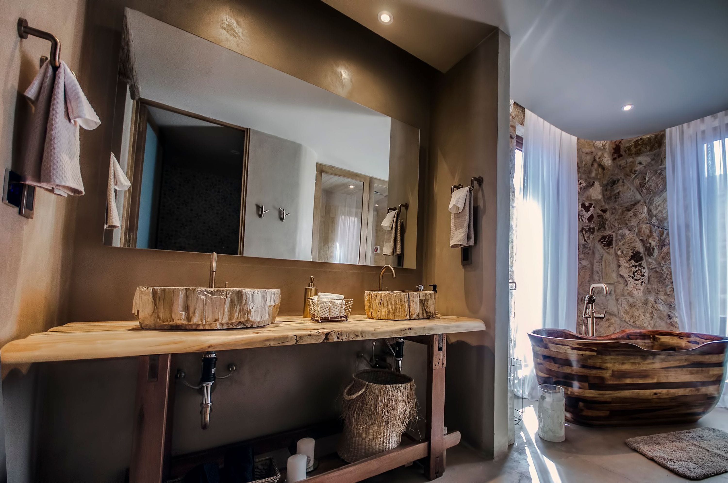 Une salle de bain moderne avec un meuble-lavabo en bois, un grand miroir, une baignoire en forme de bateau et un mur en pierre.