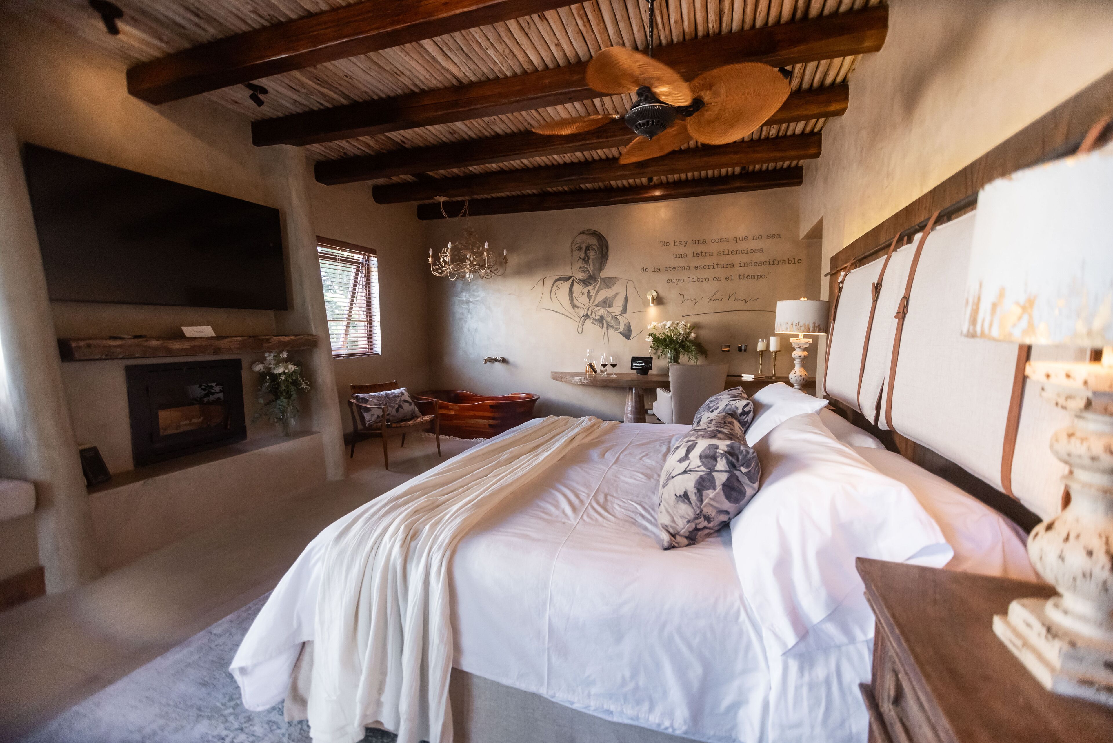 Un dormitorio con una cama grande, una chimenea, un ventilador de techo y una pared con una cita.