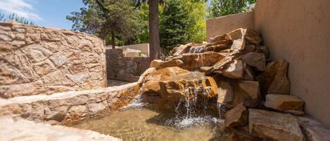 A naturalistic water feature with clear water, surrounded by large rocks and a stone wall.