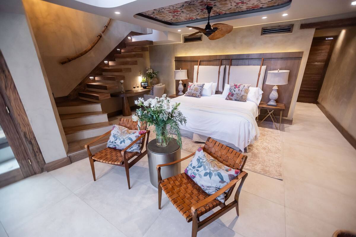 A modern bedroom with a large bed, a wooden staircase, and a seating area with chairs and a table.