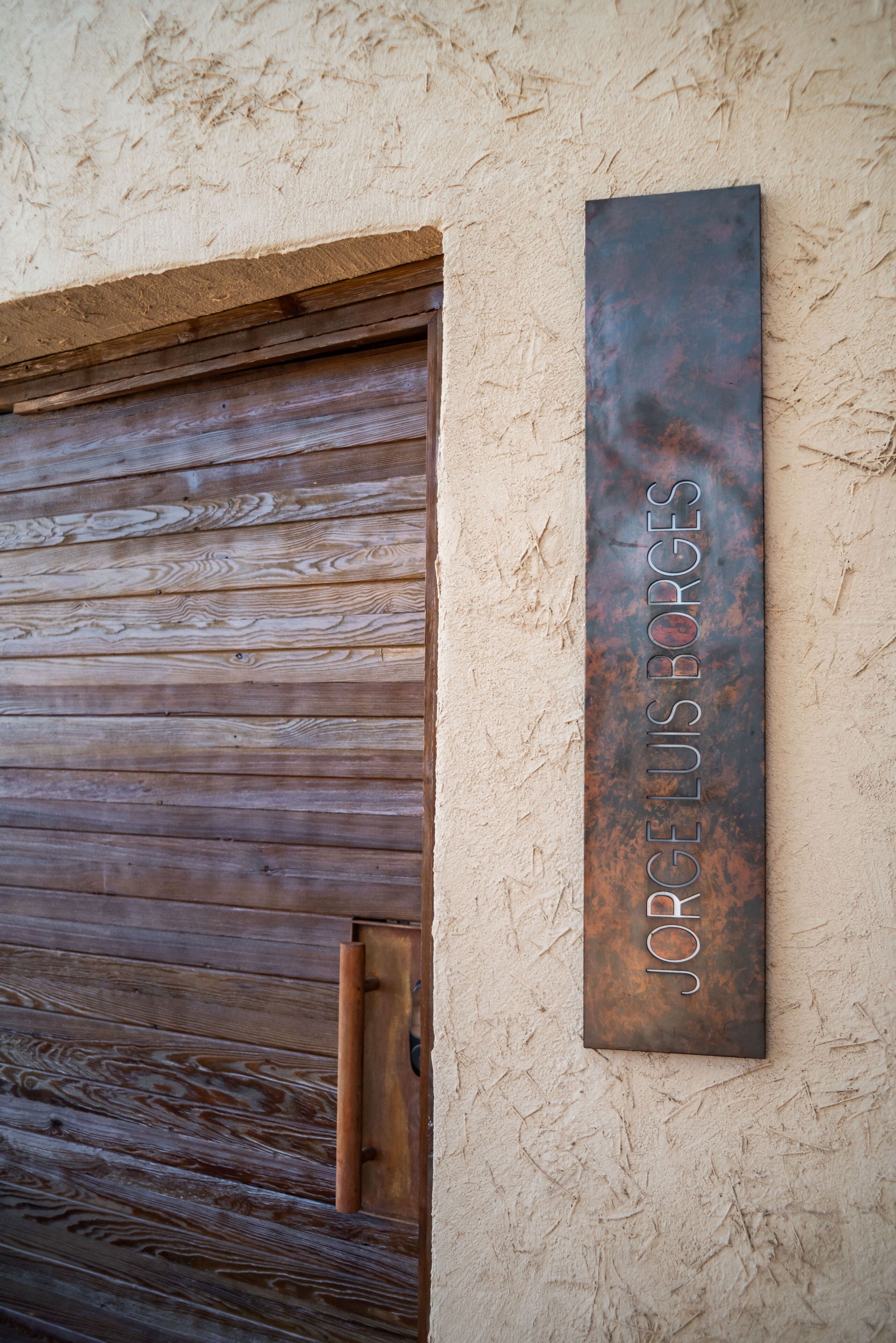 A rustic wooden door with a metal sign above it reading "Jorge Luis Borges".