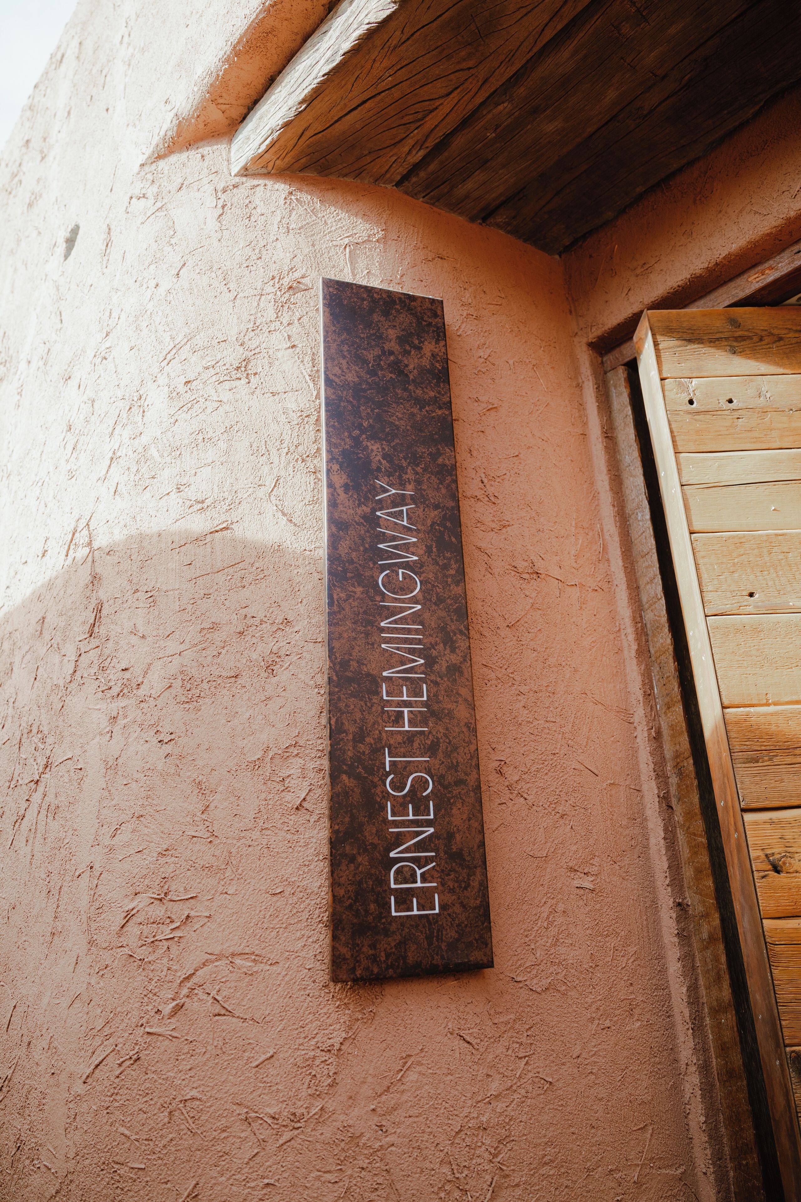 Una placa metálica vertical con la inscripción "ERNEST HEMINGWAY" fijada a una pared con textura.