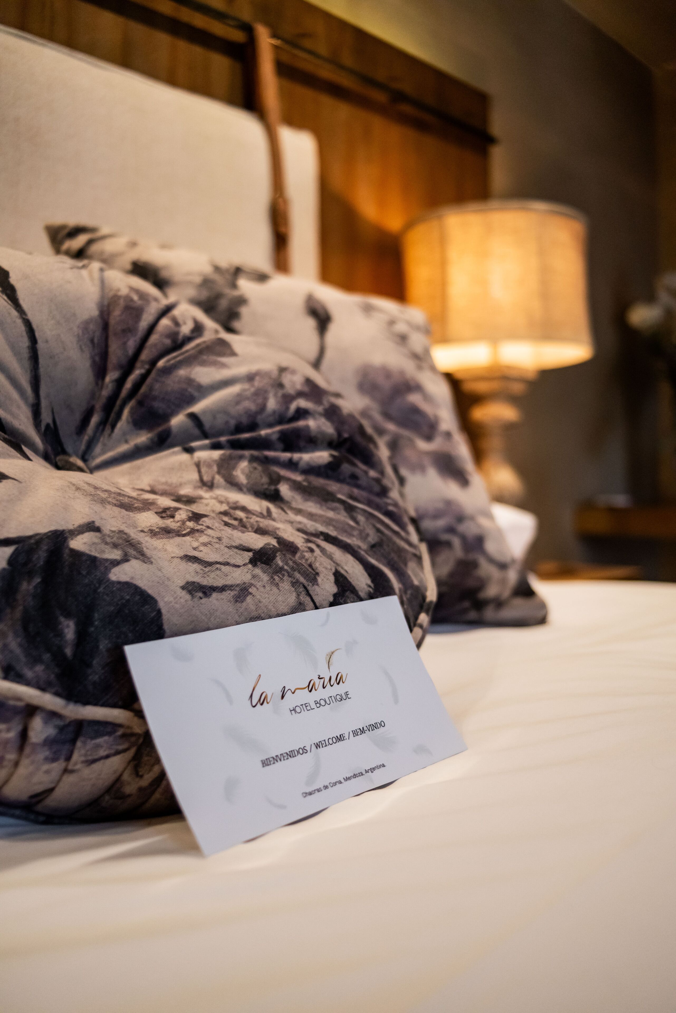 Ein Hotelzimmer mit Bett, einem floralen Kissen, einer Nachttischlampe und einer Willkommenskarte auf dem Bett.