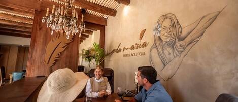 A wooden interior with a chandelier, a wall mural, and a table with people seated.