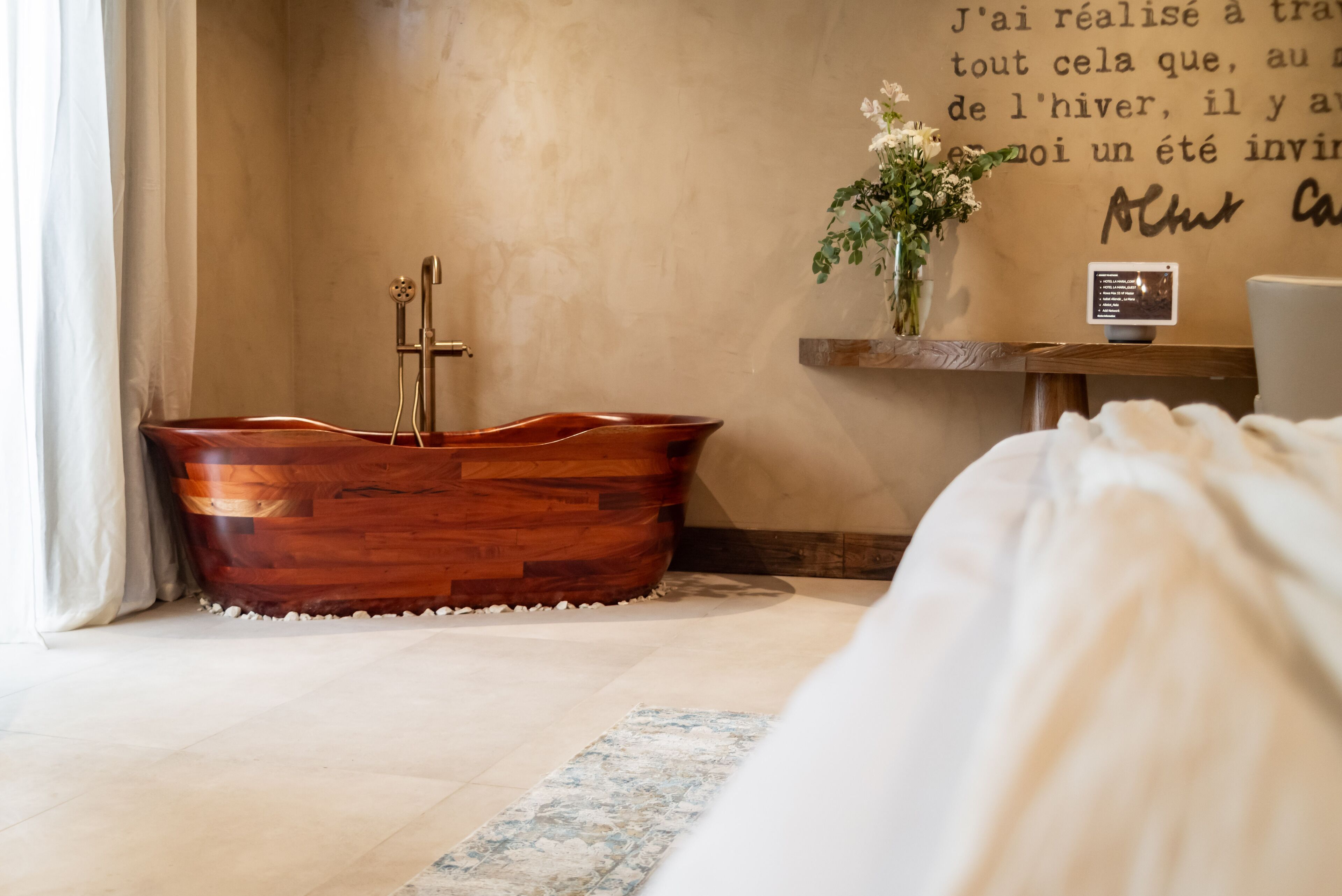 Una bañera de madera en un baño con pared color beige y un estante con un florero.