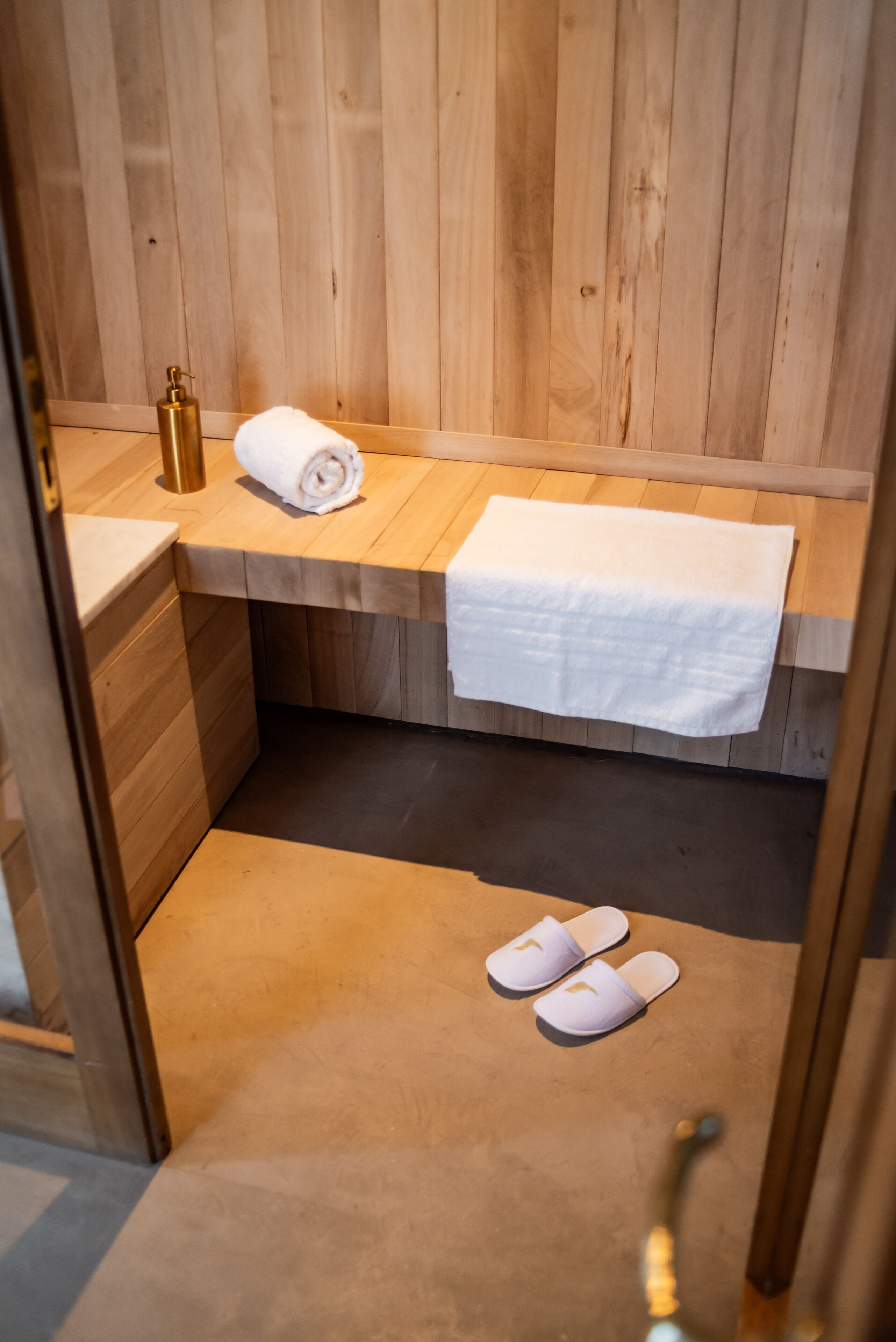 A wooden sauna room with a bench, a towel, and a bottle.