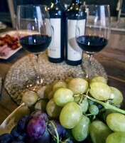 A table with two wine bottles, two wine glasses, and a plate of grapes.