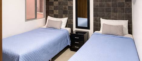 Ein Hotelzimmer mit zwei Einzelbetten, einem kleinen Schminktisch, einem Spiegel und einem Deckenventilator.