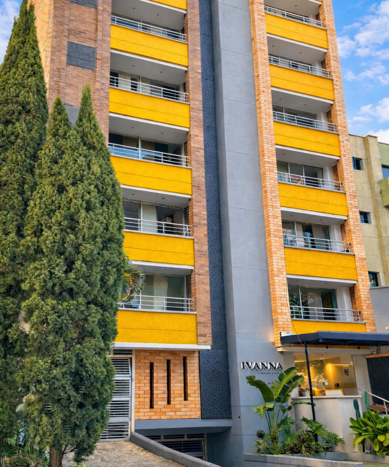 A multi-story building with yellow balconies, a visible name "IVANNA," and a large tree in the foreground.