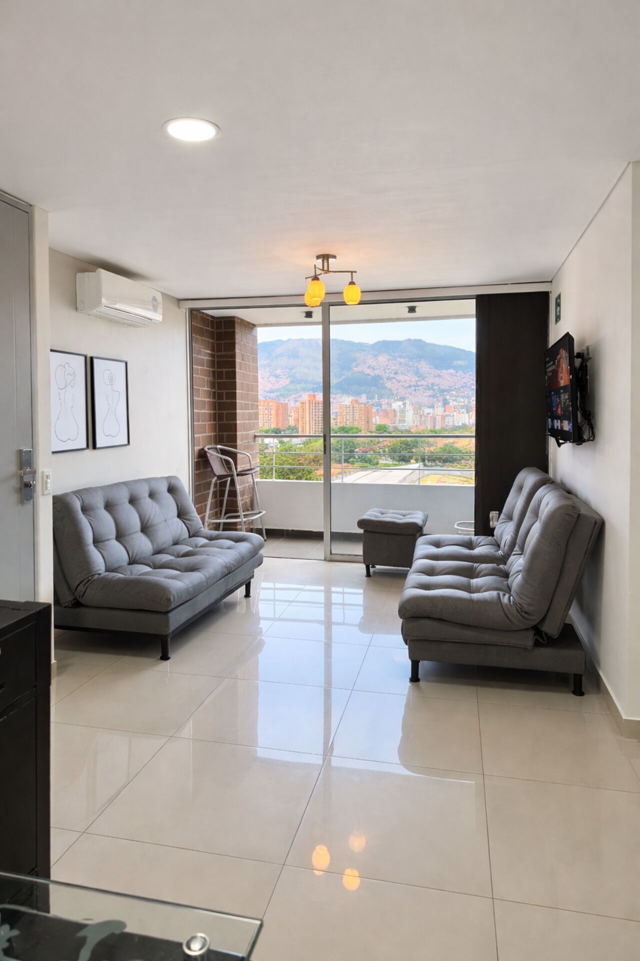 Un salon moderne avec deux canapés gris, une petite table et une vue sur le paysage urbain, visible à travers une porte vitrée.