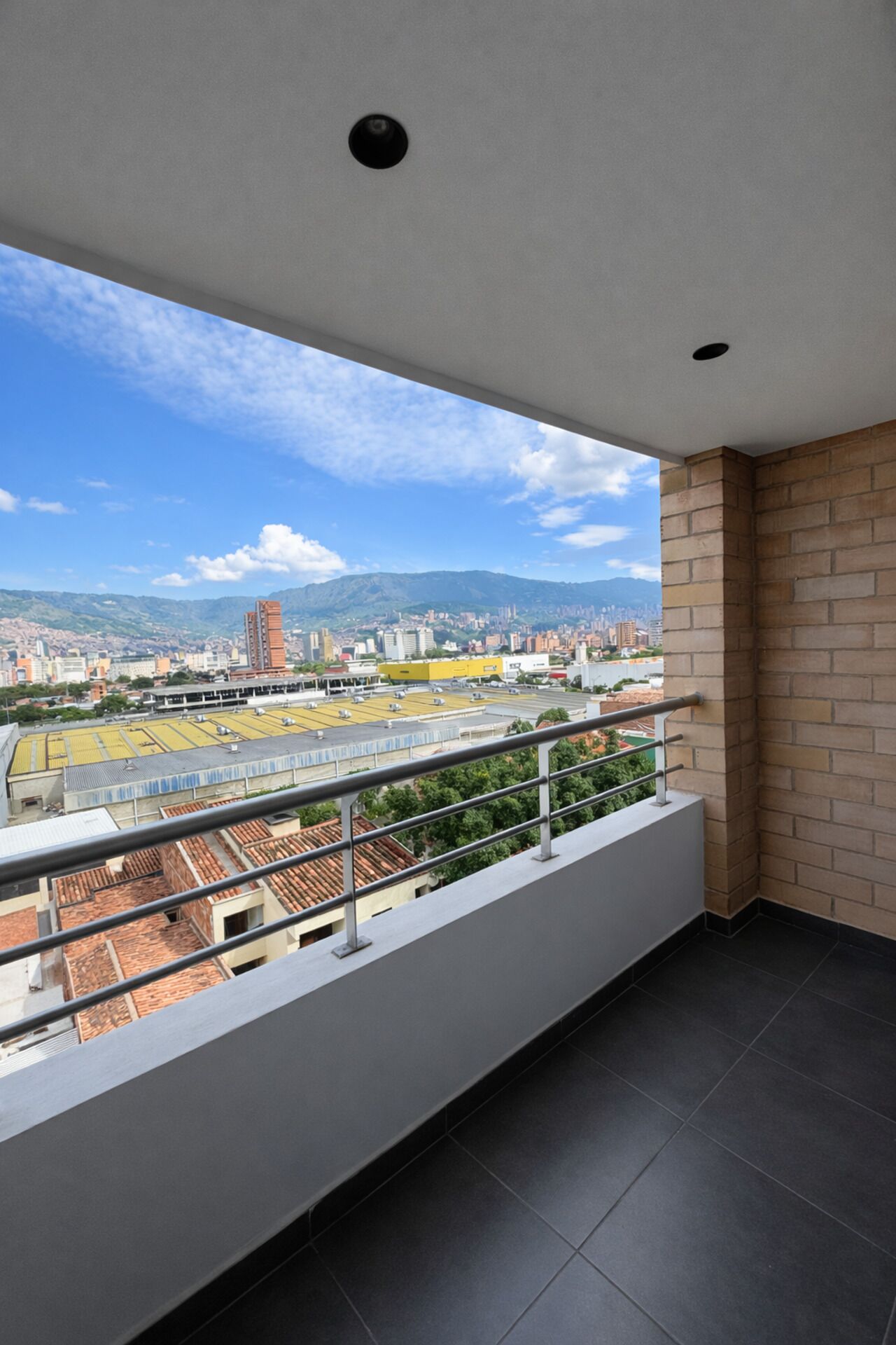 A balcony with a city view, a tiled floor, and a metal railing.