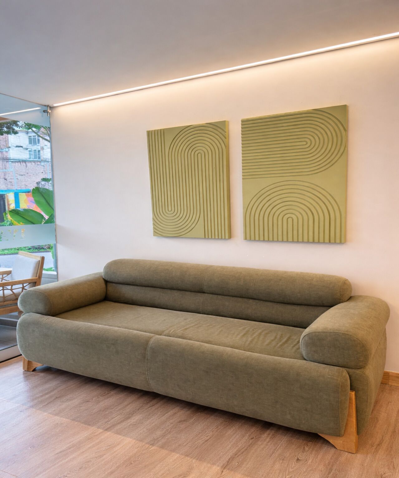 Un salón moderno con un sofá verde, dos obras de arte abstractas en la pared y suelo de madera.