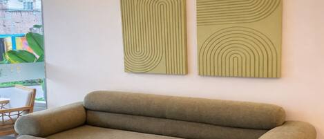 Un salón moderno con un sofá verde, dos obras de arte abstractas en la pared y suelo de madera.