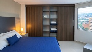 Een moderne slaapkamer met een groot bed, een inbouwkleerkast en uitzicht op de stad.