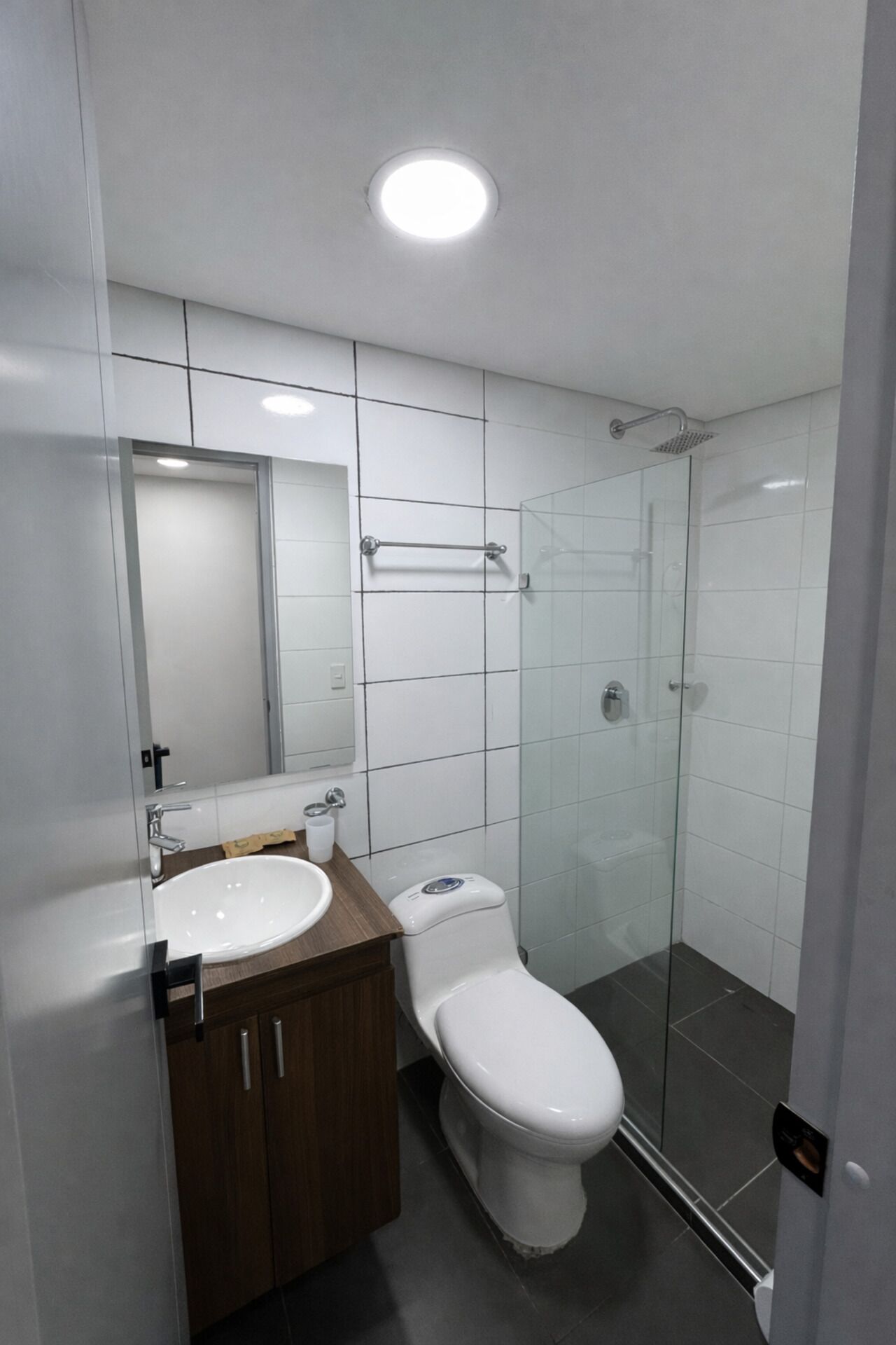 Un baño moderno con un lavamanos blanco, un inodoro, un box de ducha de vidrio y un espejo sobre el lavamanos.