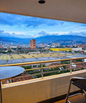 Un balcón con vistas a un paisaje urbano, incluyendo edificios y una cordillera.