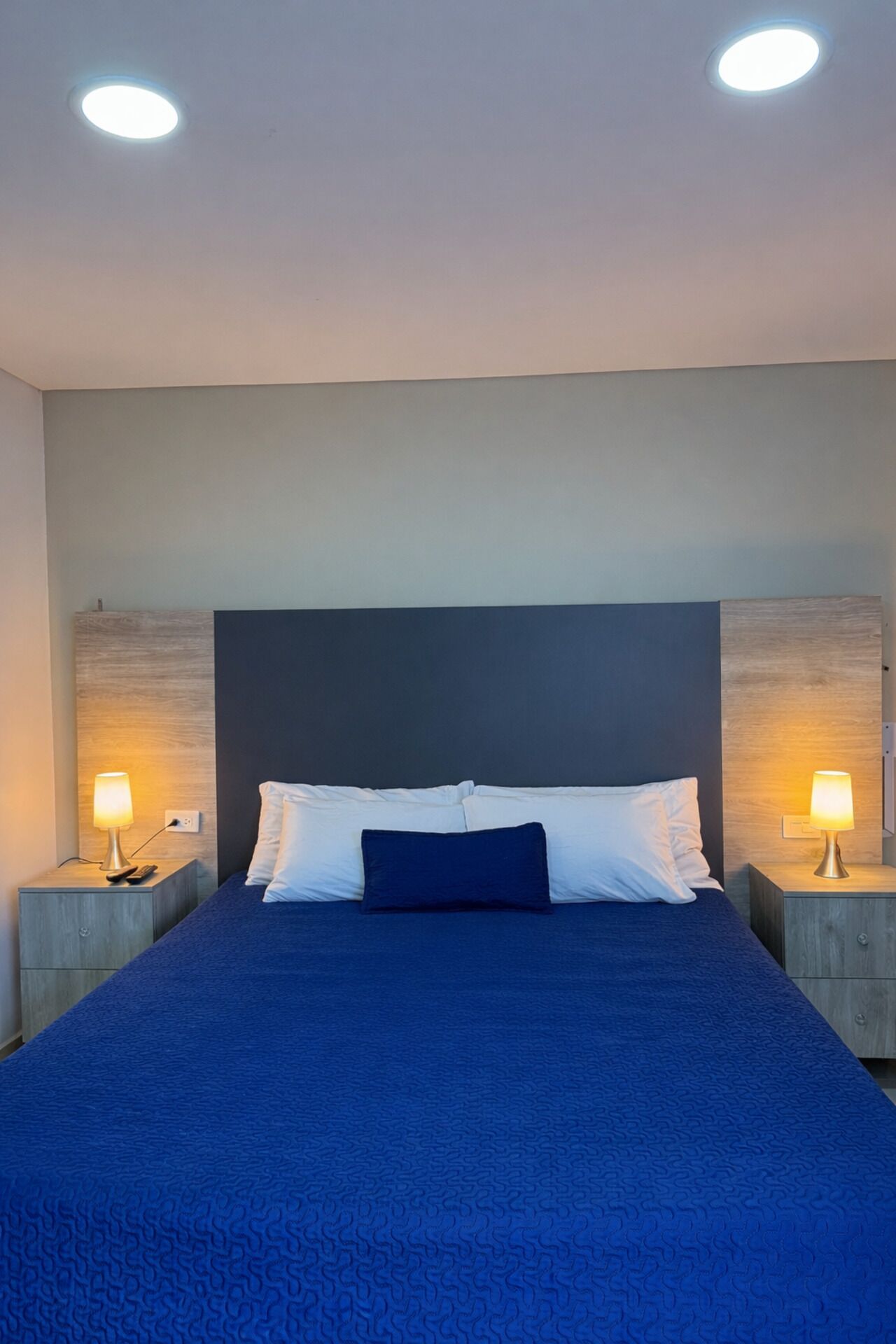 Un dormitorio con una cama grande, dos mesitas de noche con lámparas y una lámpara en el techo.