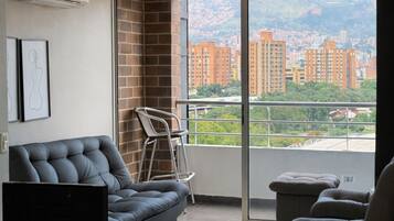 A modern living room with a sofa, a chair, a TV, and a balcony with a city view.