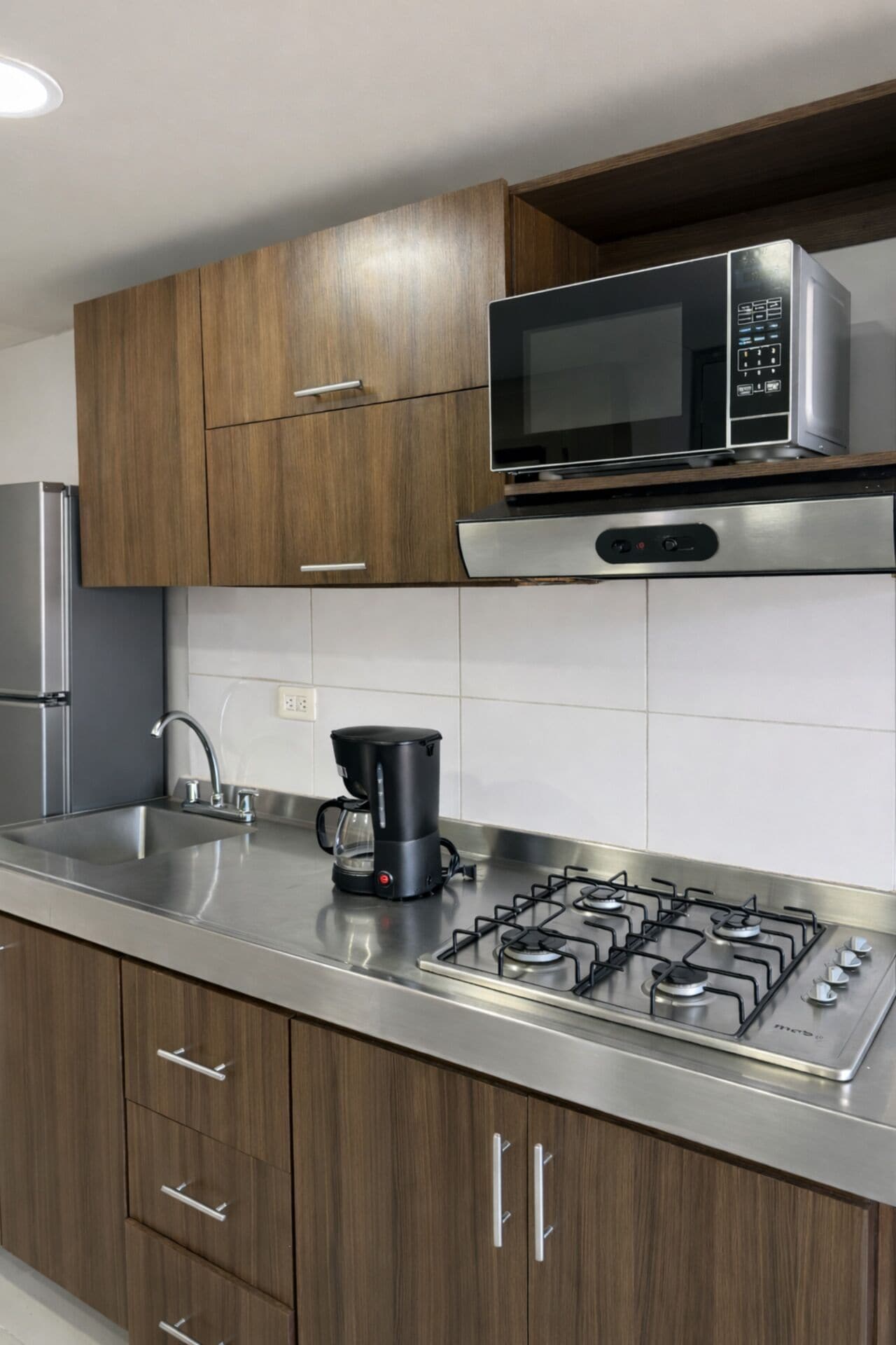 Una cocina con armarios de madera, un lavamanos de acero inoxidable, una cafetera, un microondas y una estufa a gas.