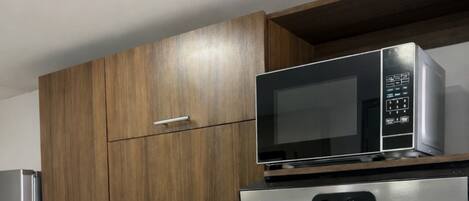 Una cocina con armarios de madera, un lavamanos de acero inoxidable, una cafetera, un microondas y una estufa a gas.