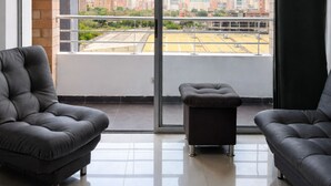 Een moderne woonkamer met twee banken, een klein poufje en een grote schuifglazen deur die leidt naar een balkon met uitzicht over de stad.