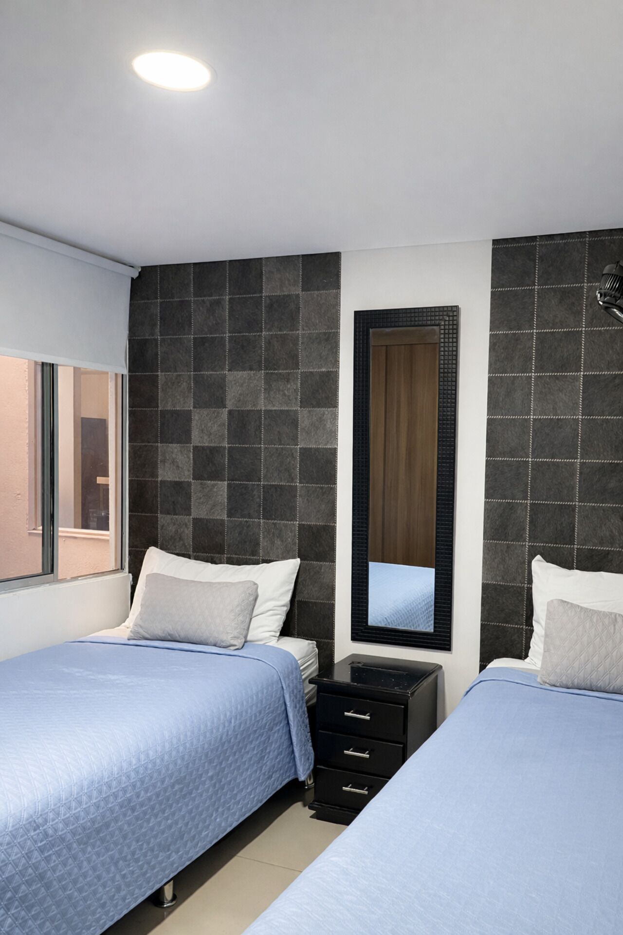 A bedroom with two beds, a nightstand, a mirror, and a window.