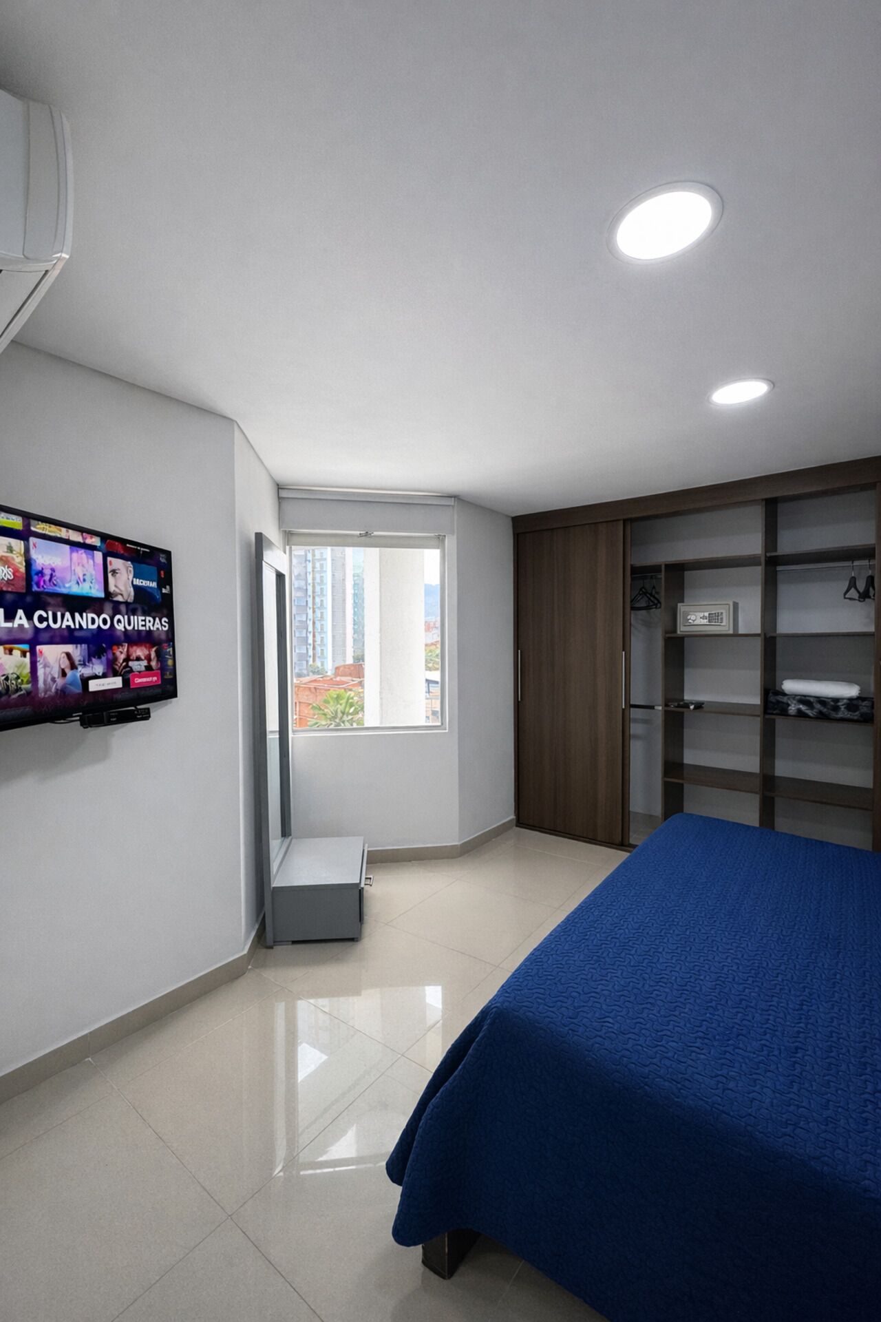 Un dormitorio con cama, televisor en la pared, armario y ventana.