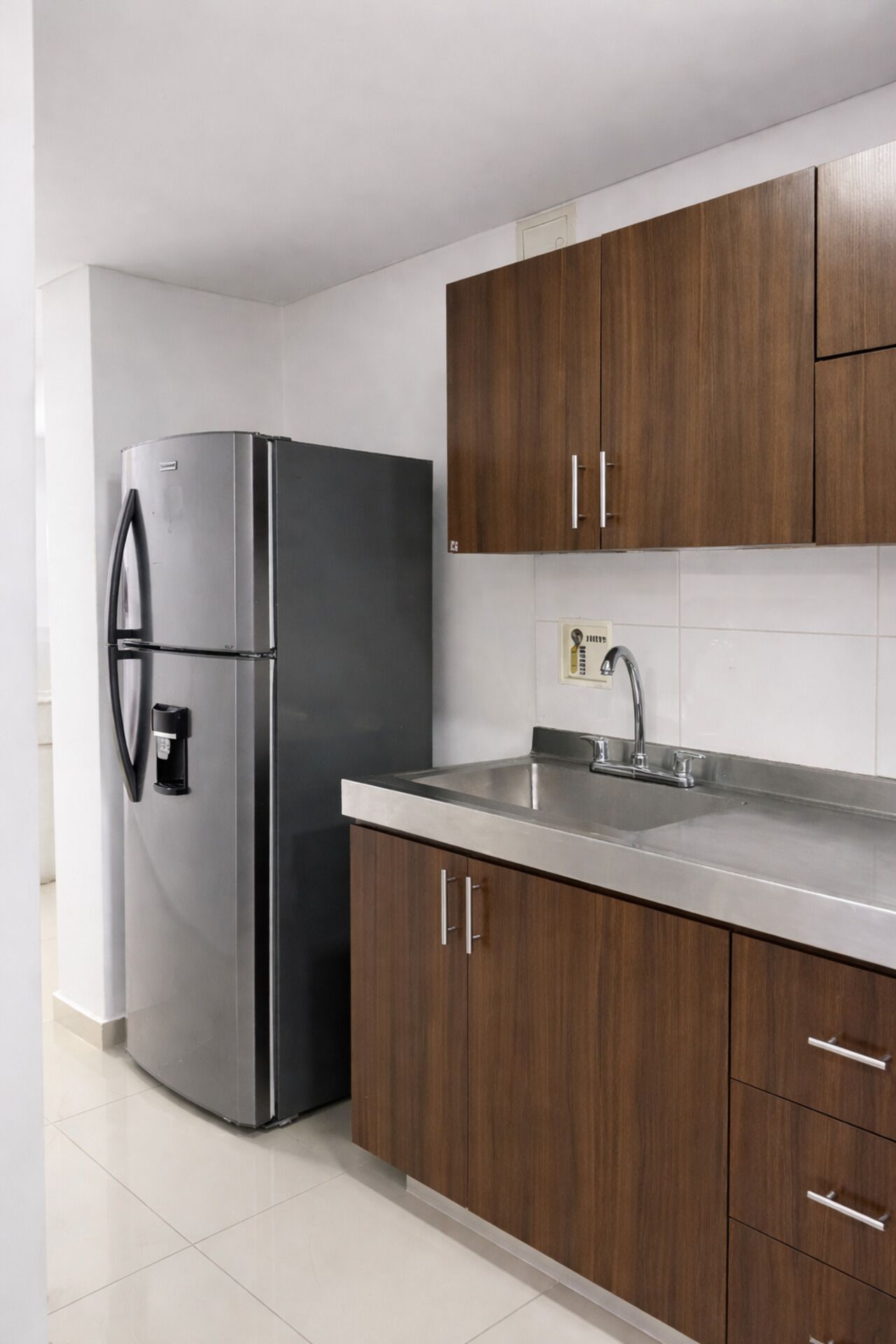 Une cuisine équipée d’un réfrigérateur en acier inoxydable, de meubles en bois, d’un évier et d’un plan de travail carrelé.