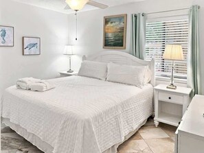 A white bed with a quilted cover, a bedside lamp, and a nightstand with a drawer.