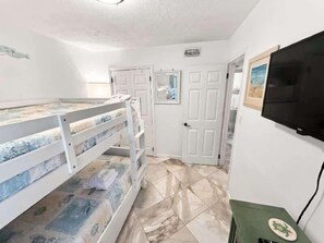 Una habitación con literas, un televisor y una puerta que da a otra habitación.