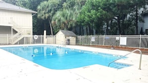 A rectangular swimming pool with a white deck and metal railings, surrounded by a white fence and palm trees.