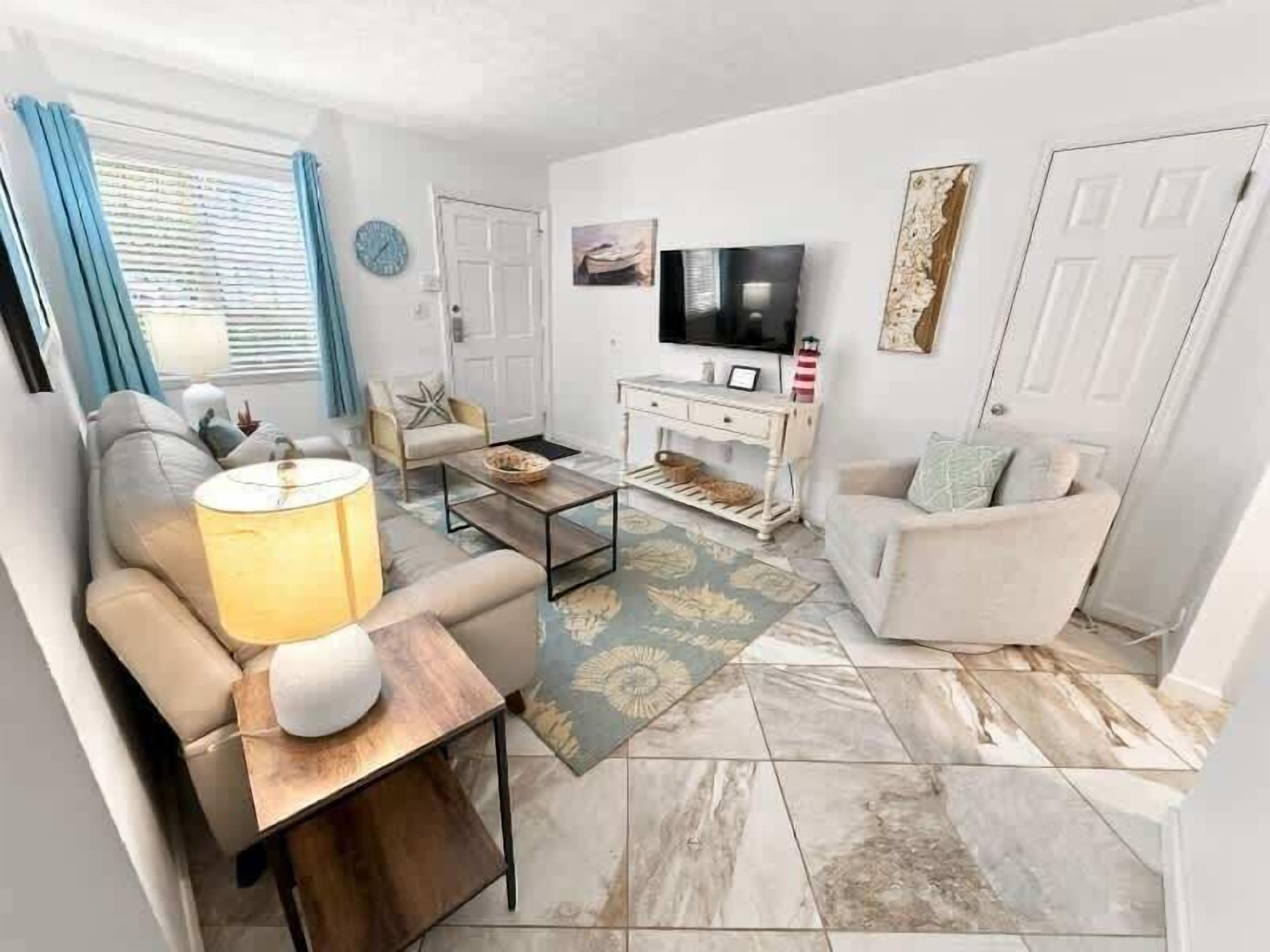 Una sala de estar con sofá, sillón, mesa de centro, televisor y objetos decorativos.