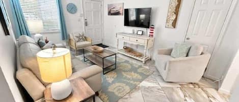 Una sala de estar con sofá, sillón, mesa de centro, televisor y objetos decorativos.