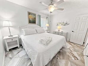 Une chambre à coucher avec un lit, une table de chevet, une lampe, un ventilateur de plafond et une porte.
