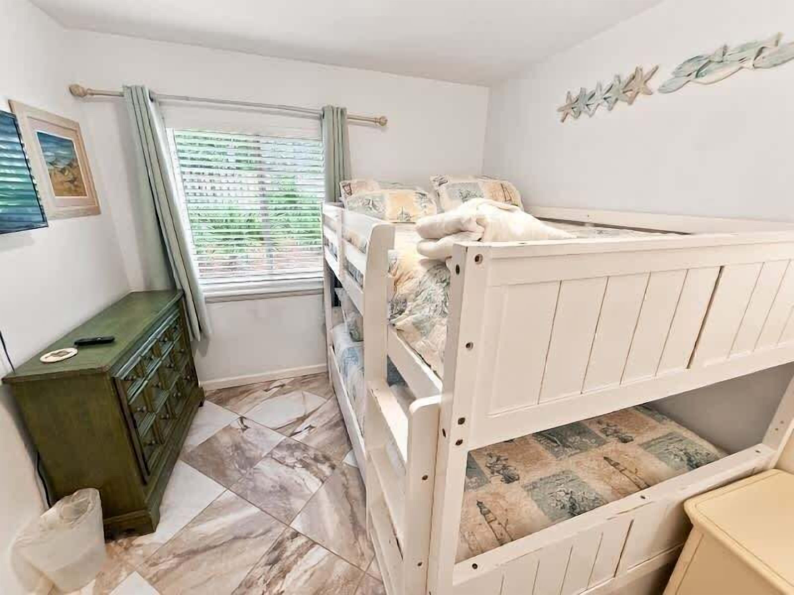 Uma cama beliche infantil com estrutura de madeira, cômoda e janela com persianas.
