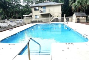 A rectangular swimming pool with a metal ladder in the foreground, surrounded by a white fence.