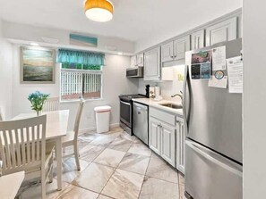 Una cocina con armarios blancos, un refrigerador de acero inoxidable y piso de baldosas.