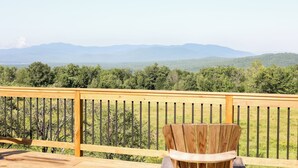 A wooden deck with a wooden chair, overlooking a forested landscape with distant mountains. - Dog Friendly, Modern Retreat w/ Stunning View (Freedom)